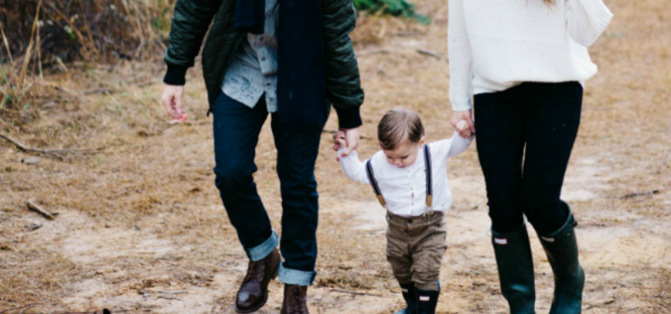 A mother and father holding hands with a toddler on a muddy walk