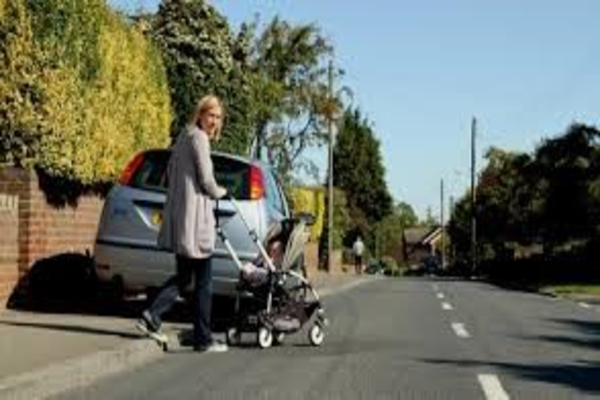 Photo of person pushing baby buggy into road as car parked on pavement