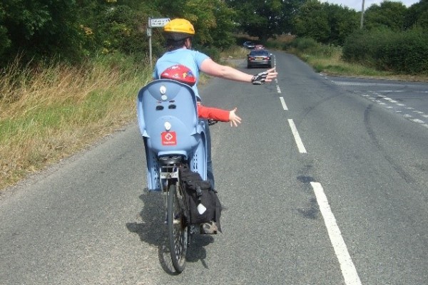 Photo of cyclist with child behind in seat. Cyclist and child passenger are indicating right turn with their arms (photo courtesy of Sustrans)
