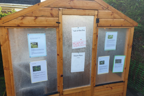 Greenhouse at Moss Rose Cottage with gardening instructions and community updates displayed on the door.